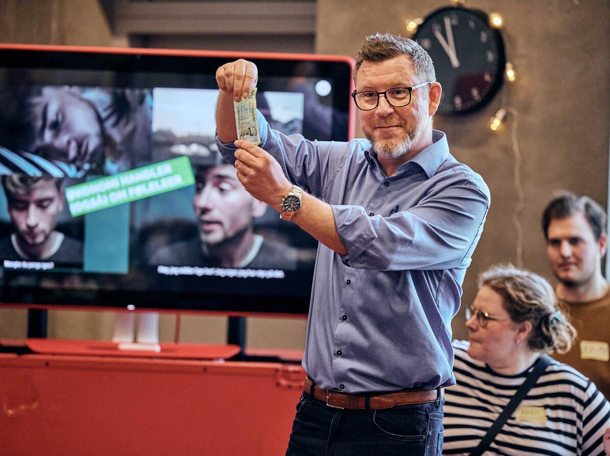 Underviser står med pengeseddel og underviser om økonomi.